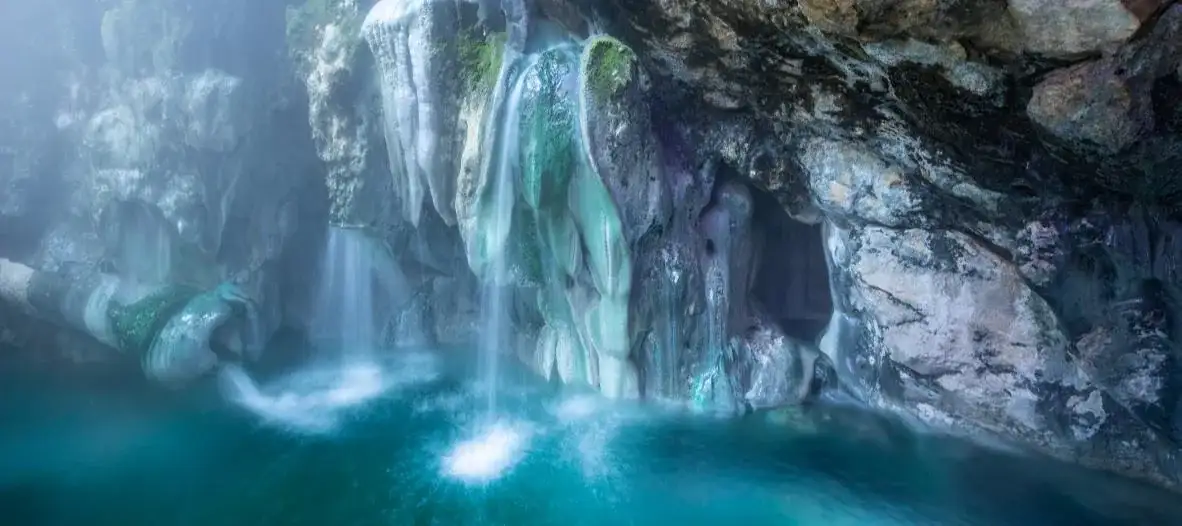 The Bibi-Fatima holy spring cascading into a turquoise pool inside a cave
