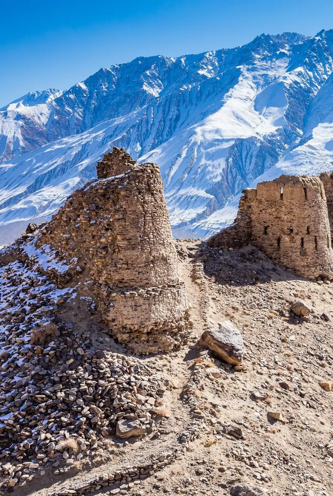 Snow-capped Pamir peaks rising behind a crumbling fortress tower